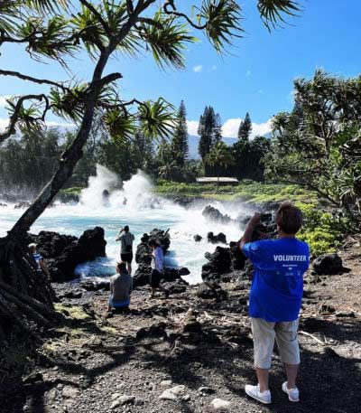 A man wearing a blue shirt that says pioneer takes a picture of the ocean