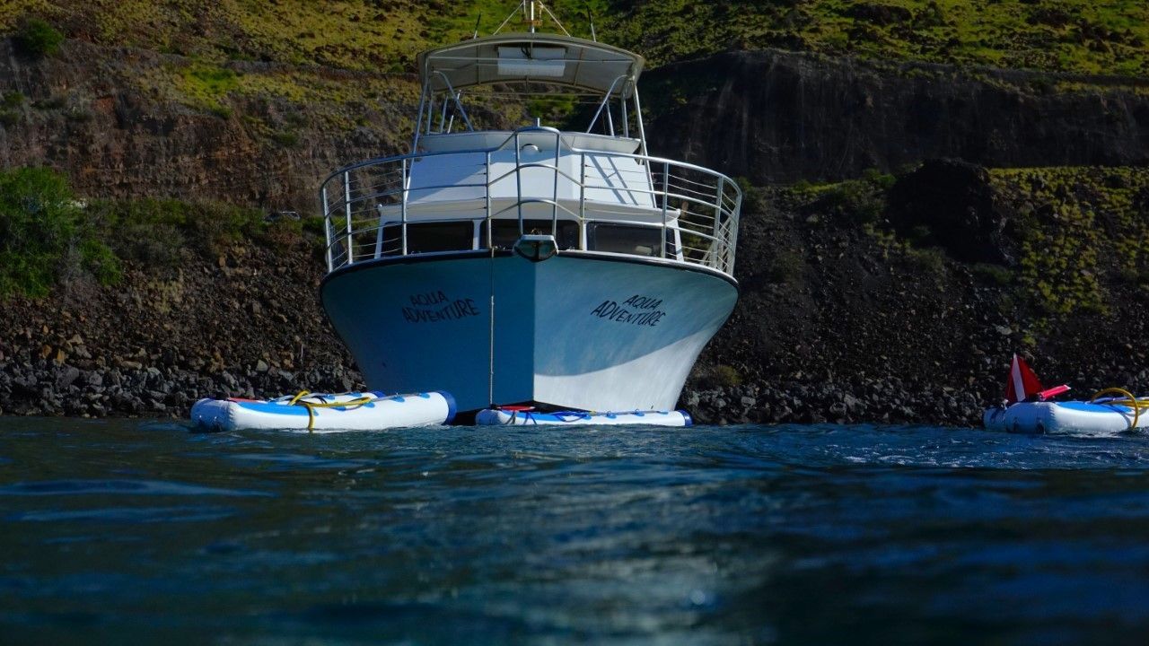 A boat is floating on top of a body of water next to a cliff.