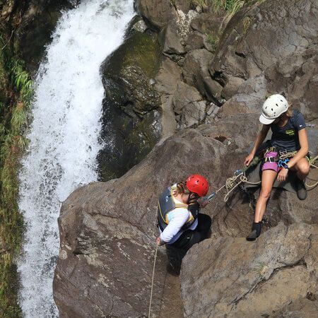A man and a woman are sitting on a rock near a waterfall.