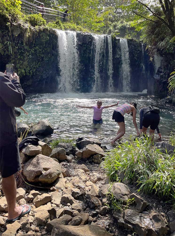 A group of people are standing in front of a waterfall.