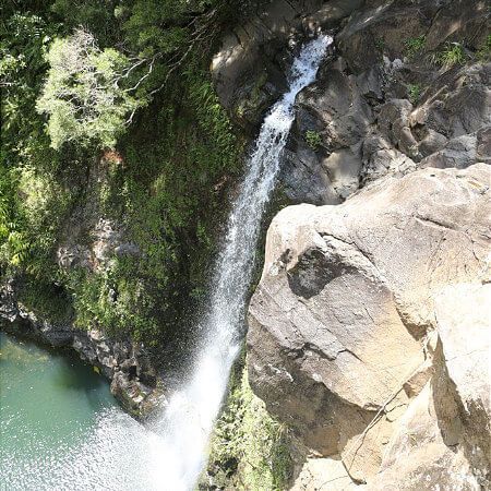 A waterfall is coming down a rocky cliff into a body of water.