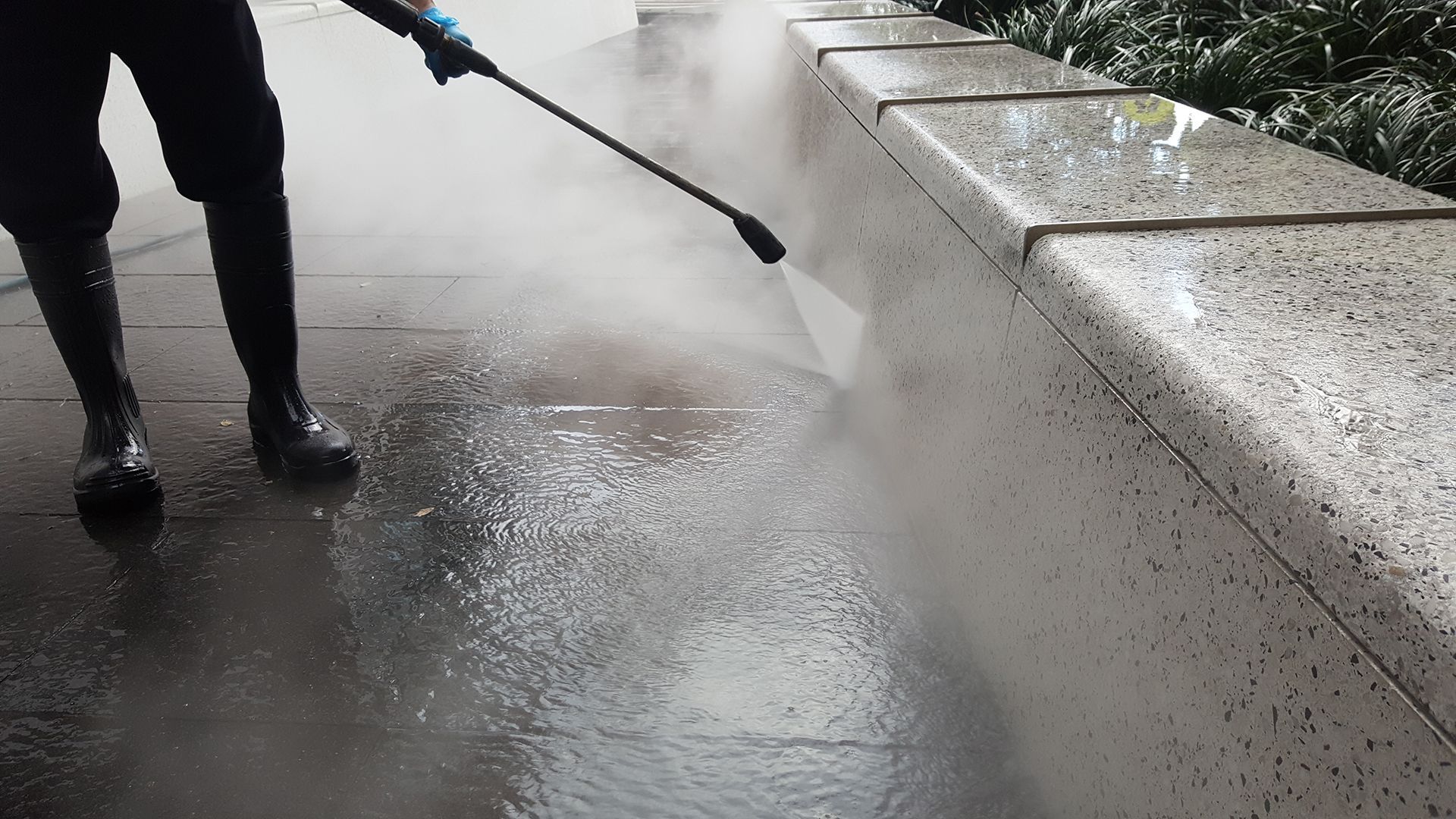A person is using a high pressure washer to clean a sidewalk.