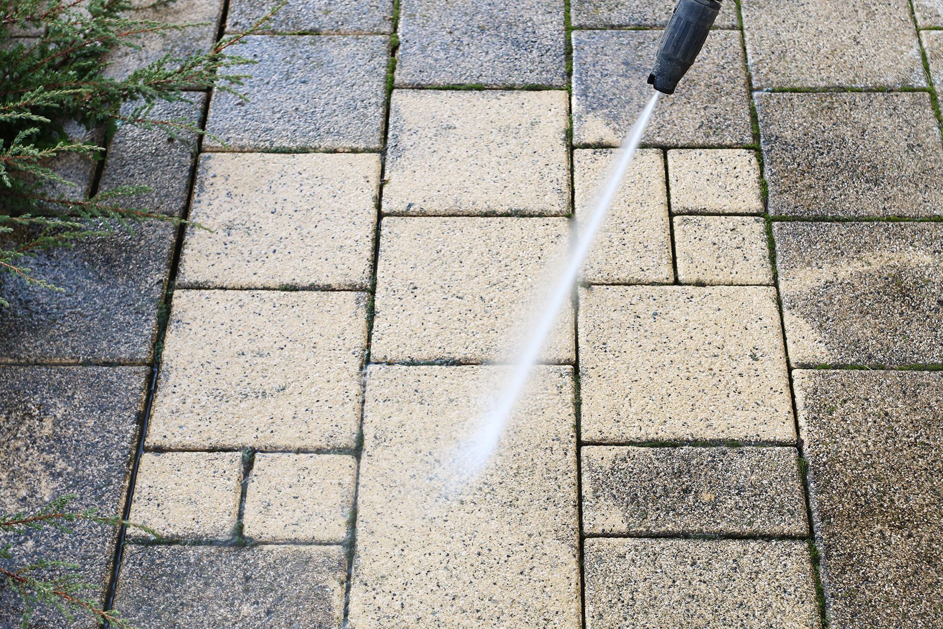 A person is using a high pressure washer to clean a brick walkway.