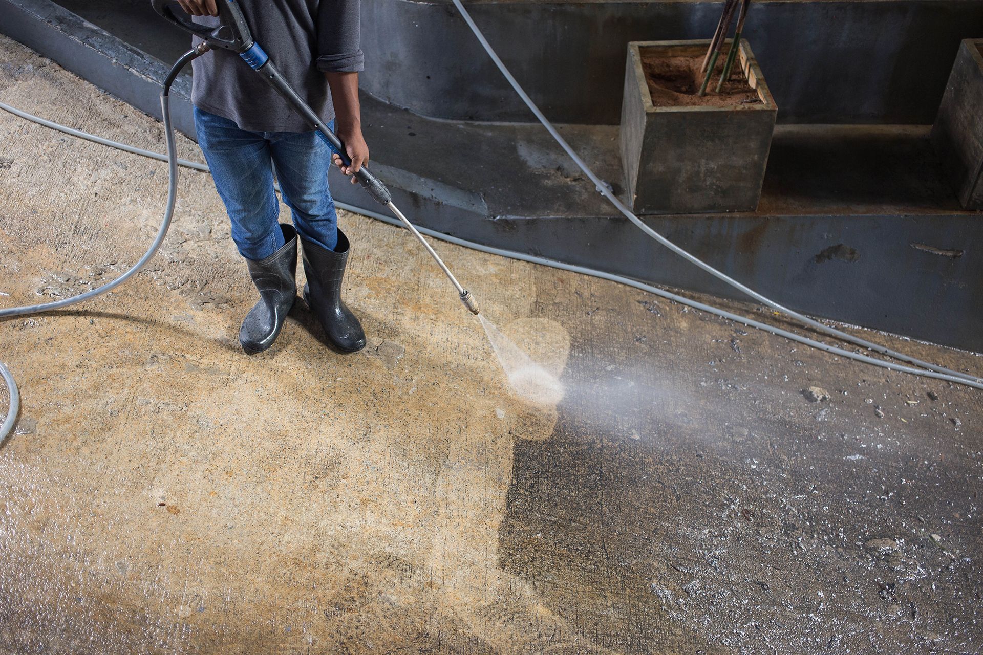 A man is using a high pressure washer to clean a concrete floor.