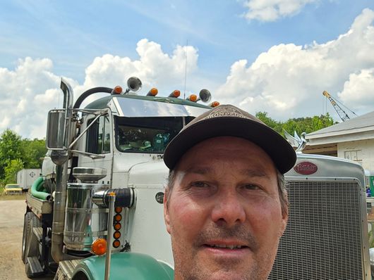 A man wearing a hat is standing in front of a semi truck.