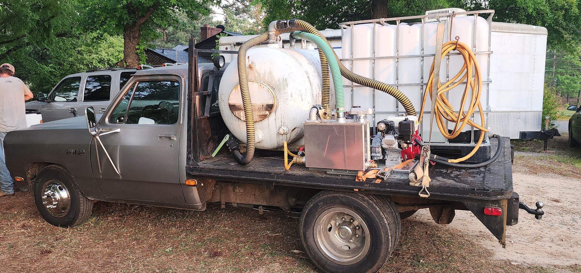 A truck with a large tank on the back is parked in the dirt.