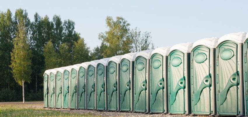 A row of portable toilets are lined up in a field.