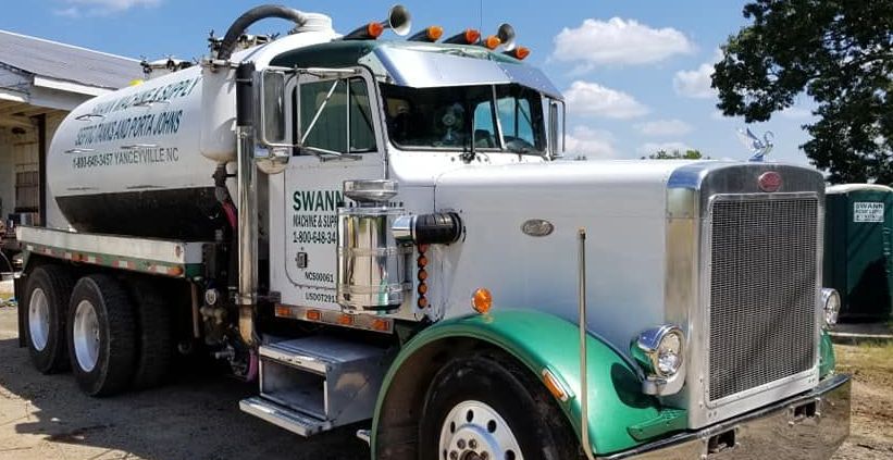 A white and green vacuum truck is parked in front of a building