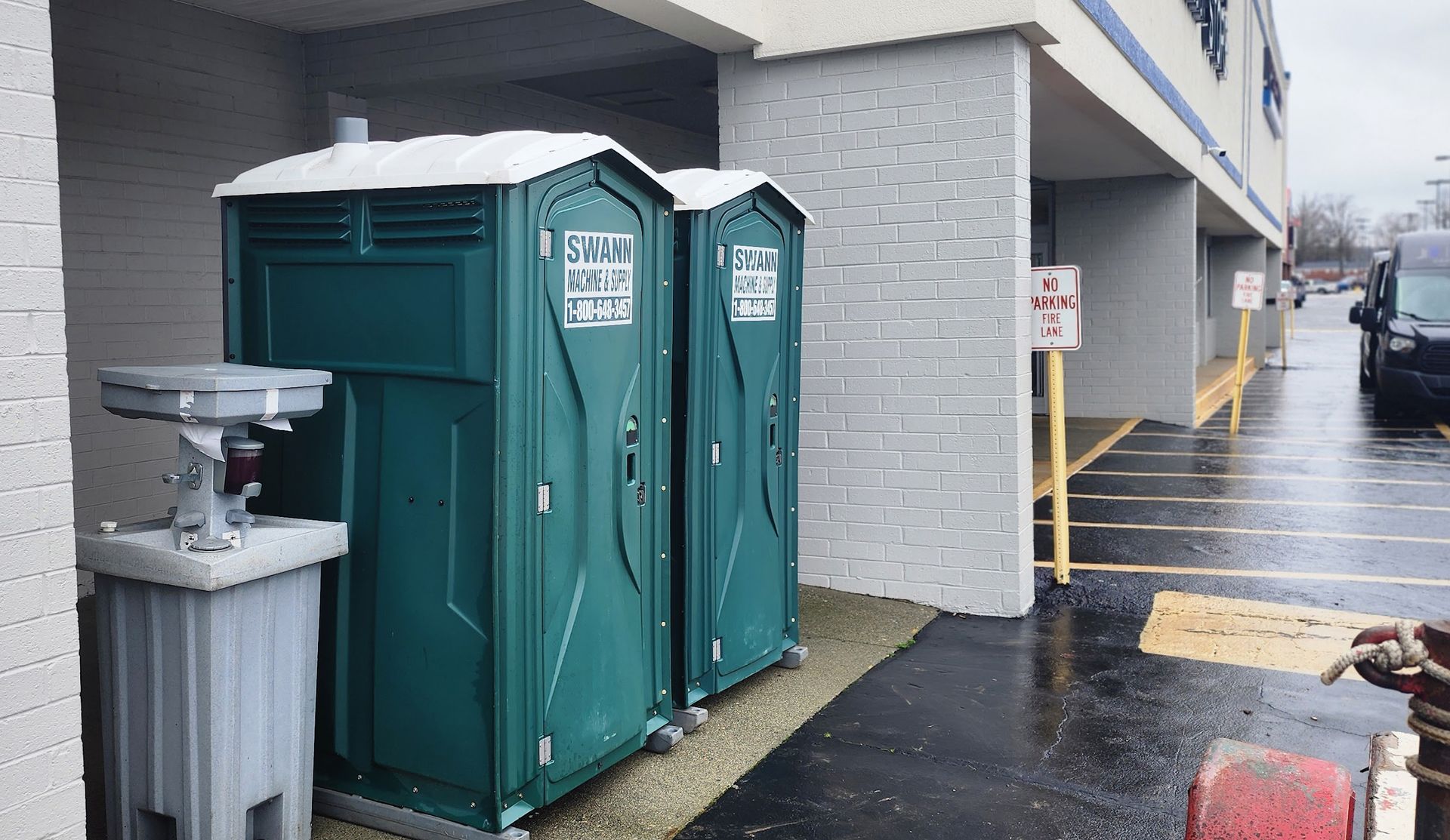 Two green portable toilets are parked outside of a building