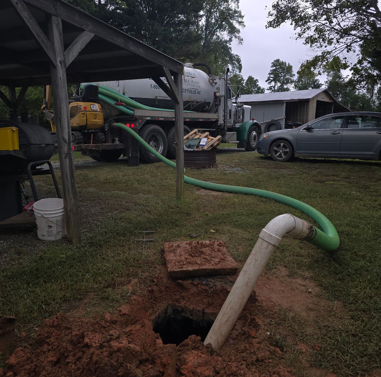 A septic tank is being pumped out by a truck with a green hose attached to it.