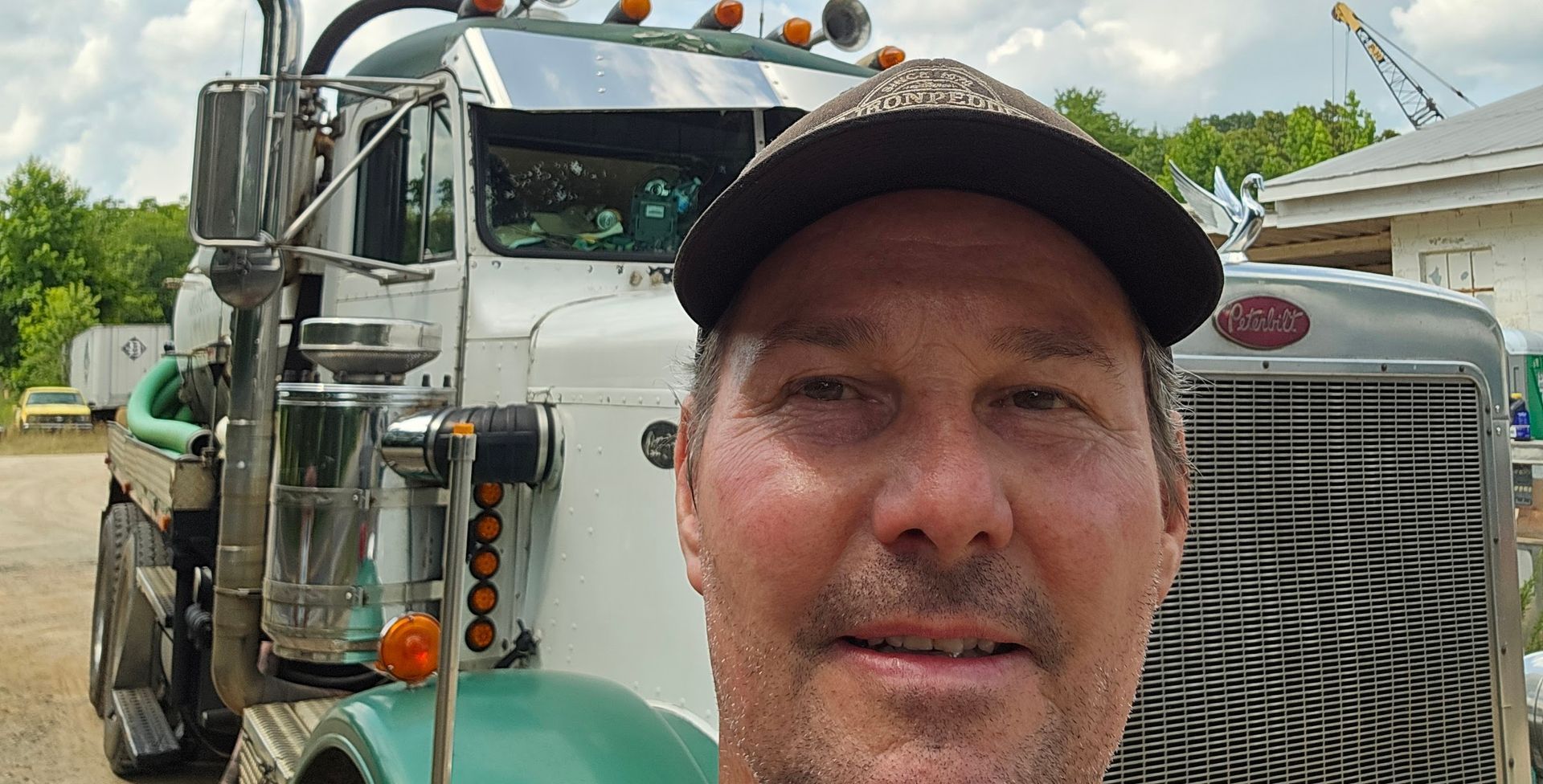 A man wearing a hat is standing in front of a semi truck.