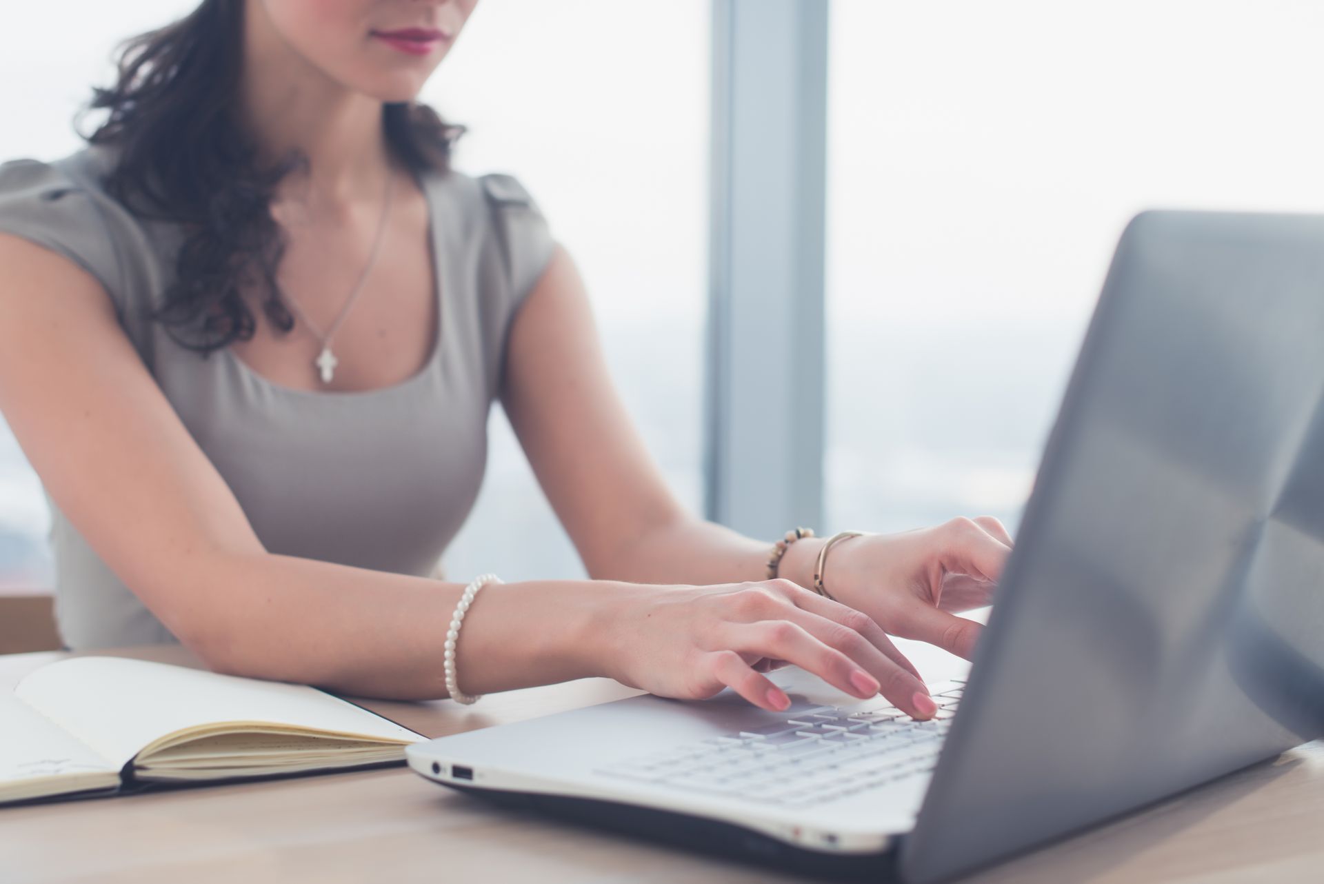A woman is typing on a laptop computer while sitting at a desk.