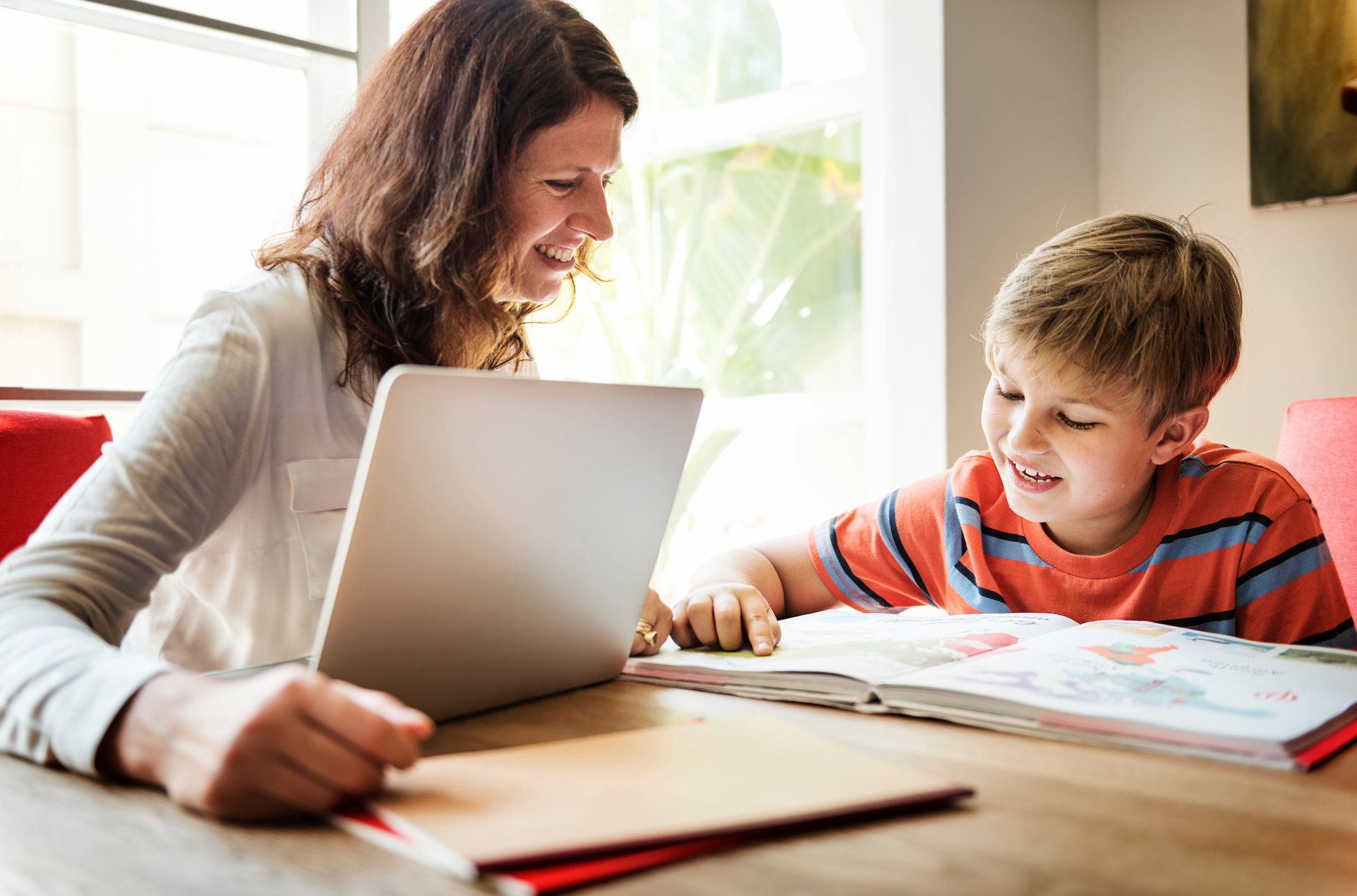 A woman is helping a young boy with his homework by using a laptop computer.