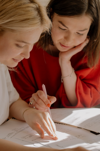Two women are sitting at a table writing on a piece of paper.