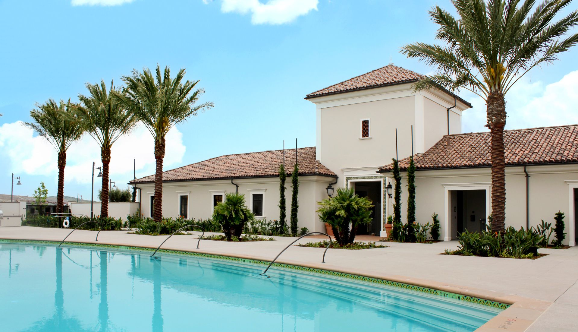 Pool overlooking a lake and hills. Teal water, light brown concrete, cloudy sky.