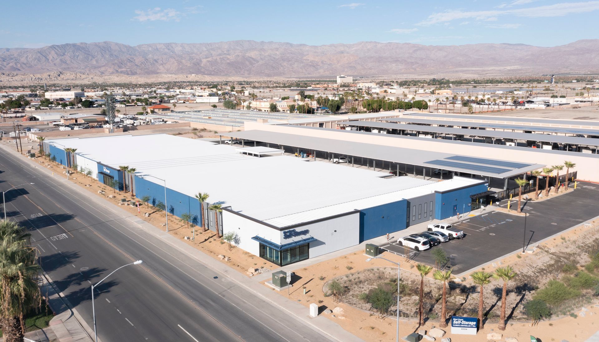 Large warehouse with blue and white facade, palm trees, and mountains in the background.