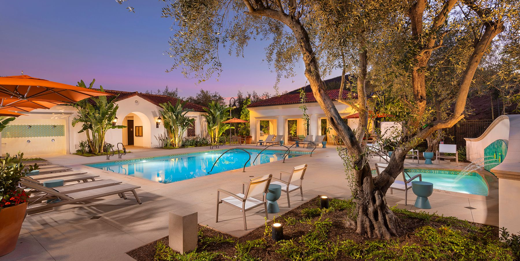 Pool overlooking a lake and hills. Teal water, light brown concrete, cloudy sky.