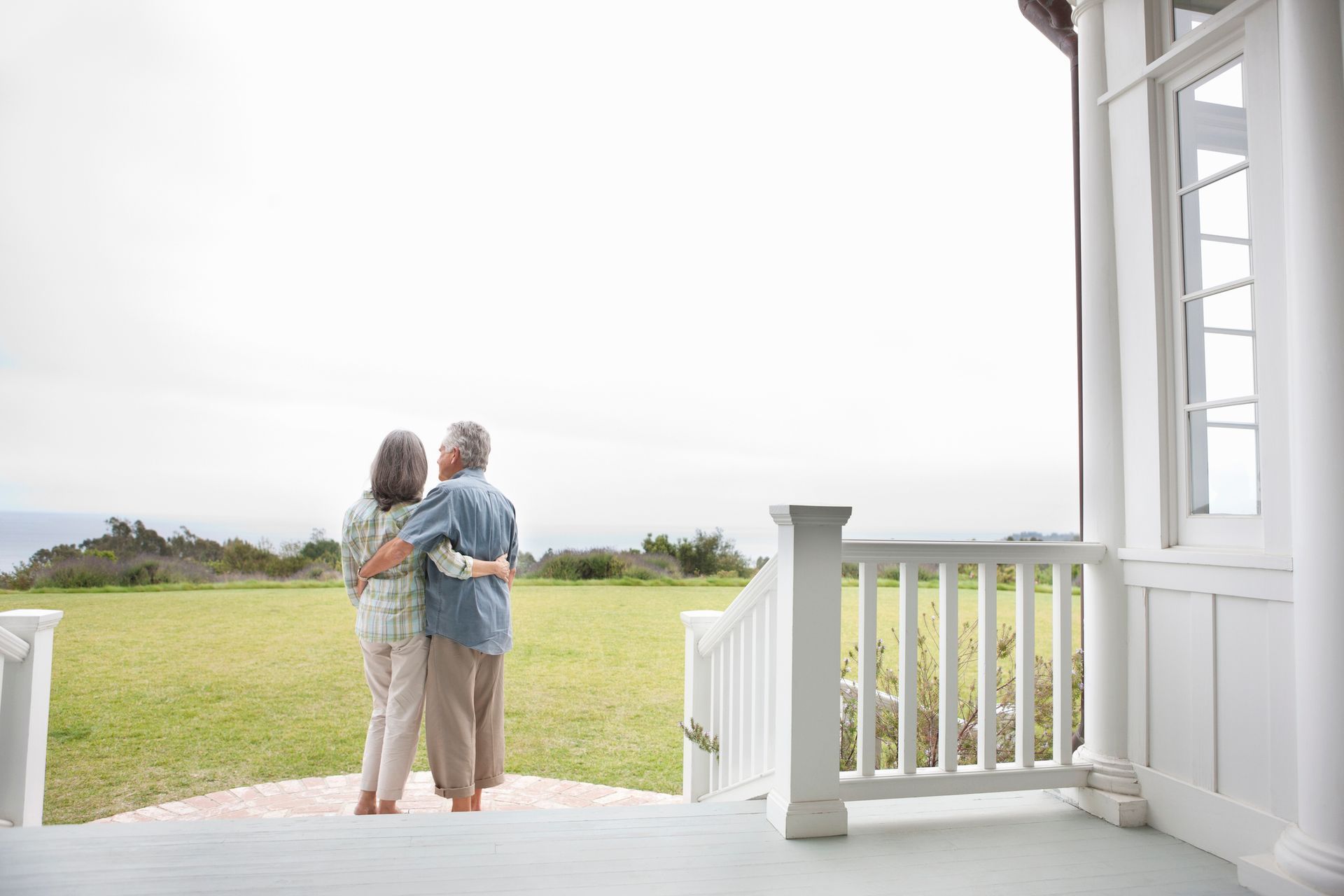 Couple with arms around each other, standing on a porch overlooking a green field and cloudy sky. Couple with arms around each other, standing on a porch overlooking a green field and cloudy sky.