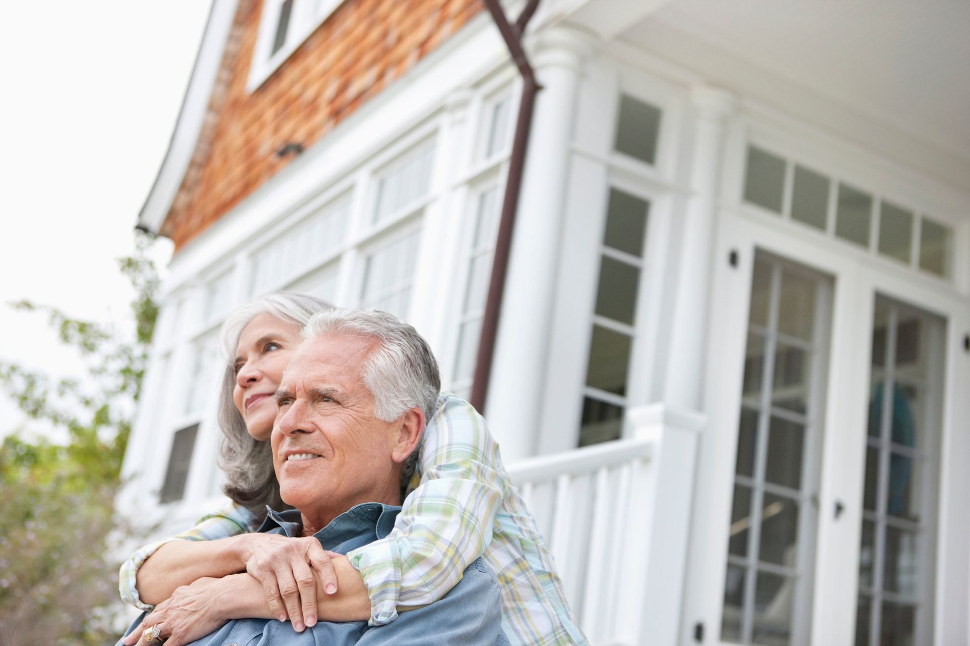 A senior couple hugs while sitting outside, in front of a blurry house. A senior couple hugs while sitting outside, in front of a blurry house.
