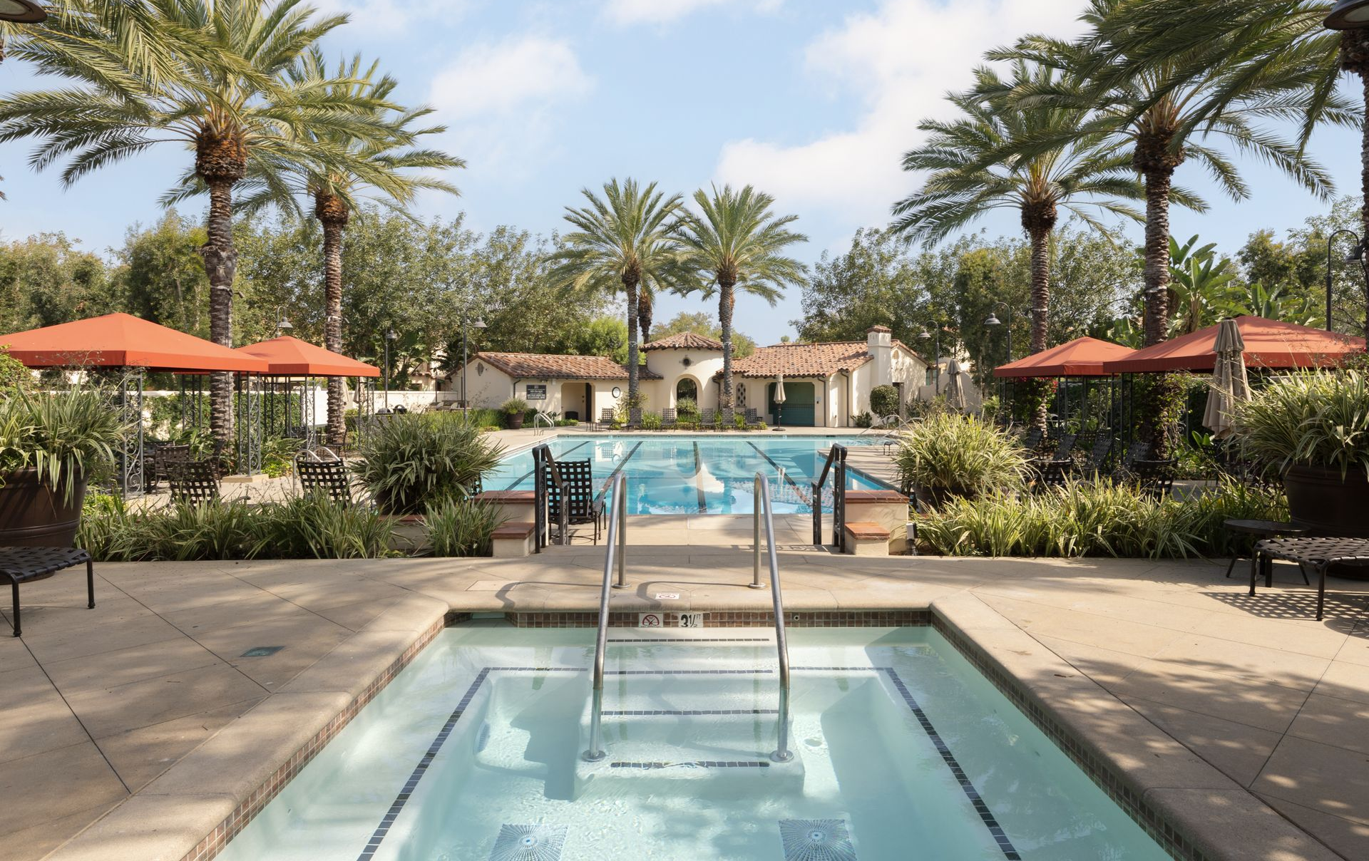 Pool overlooking a lake and hills. Teal water, light brown concrete, cloudy sky.