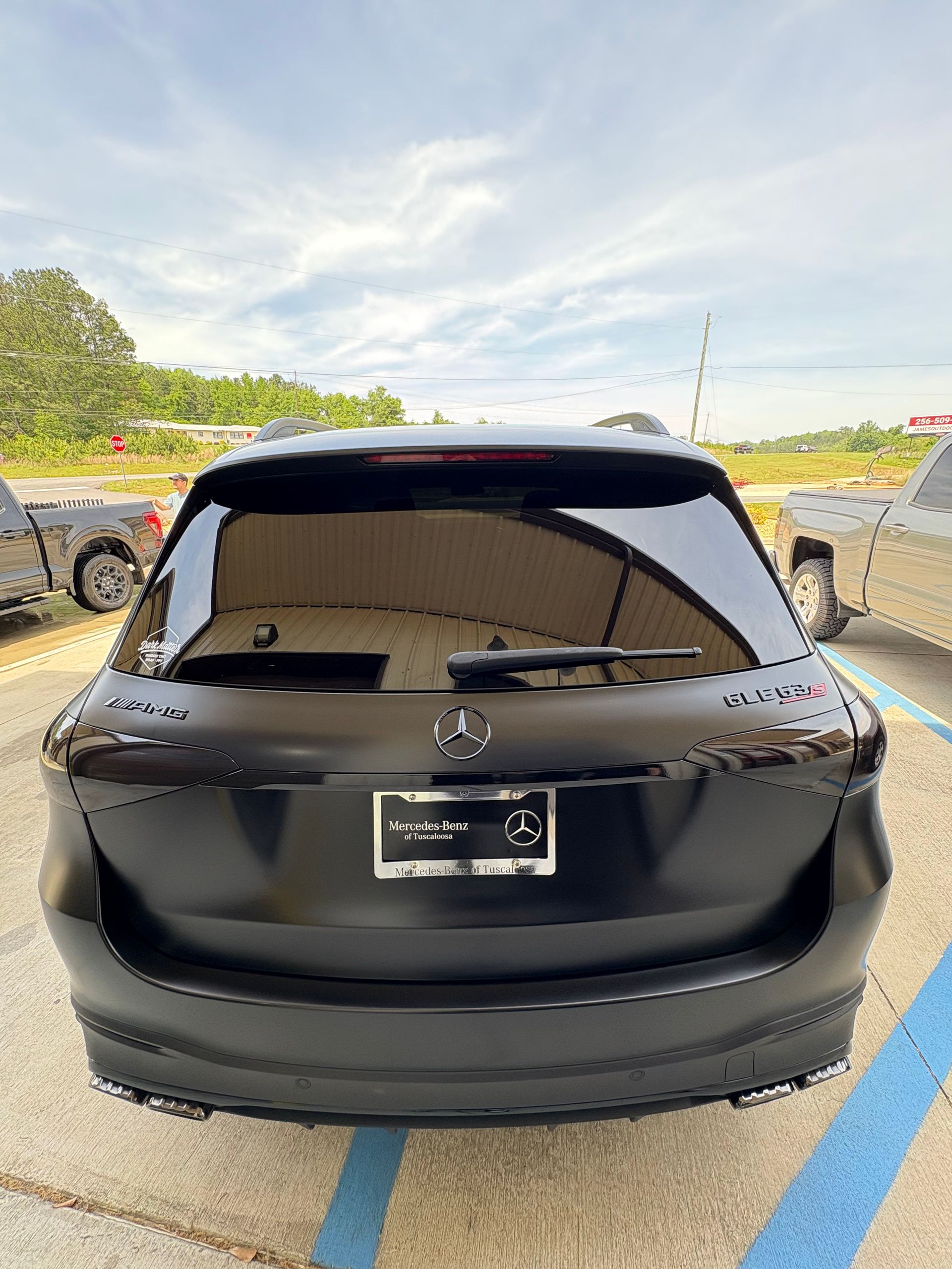 Black Mercedes SUV, rear view, parked outdoors under cloudy sky.