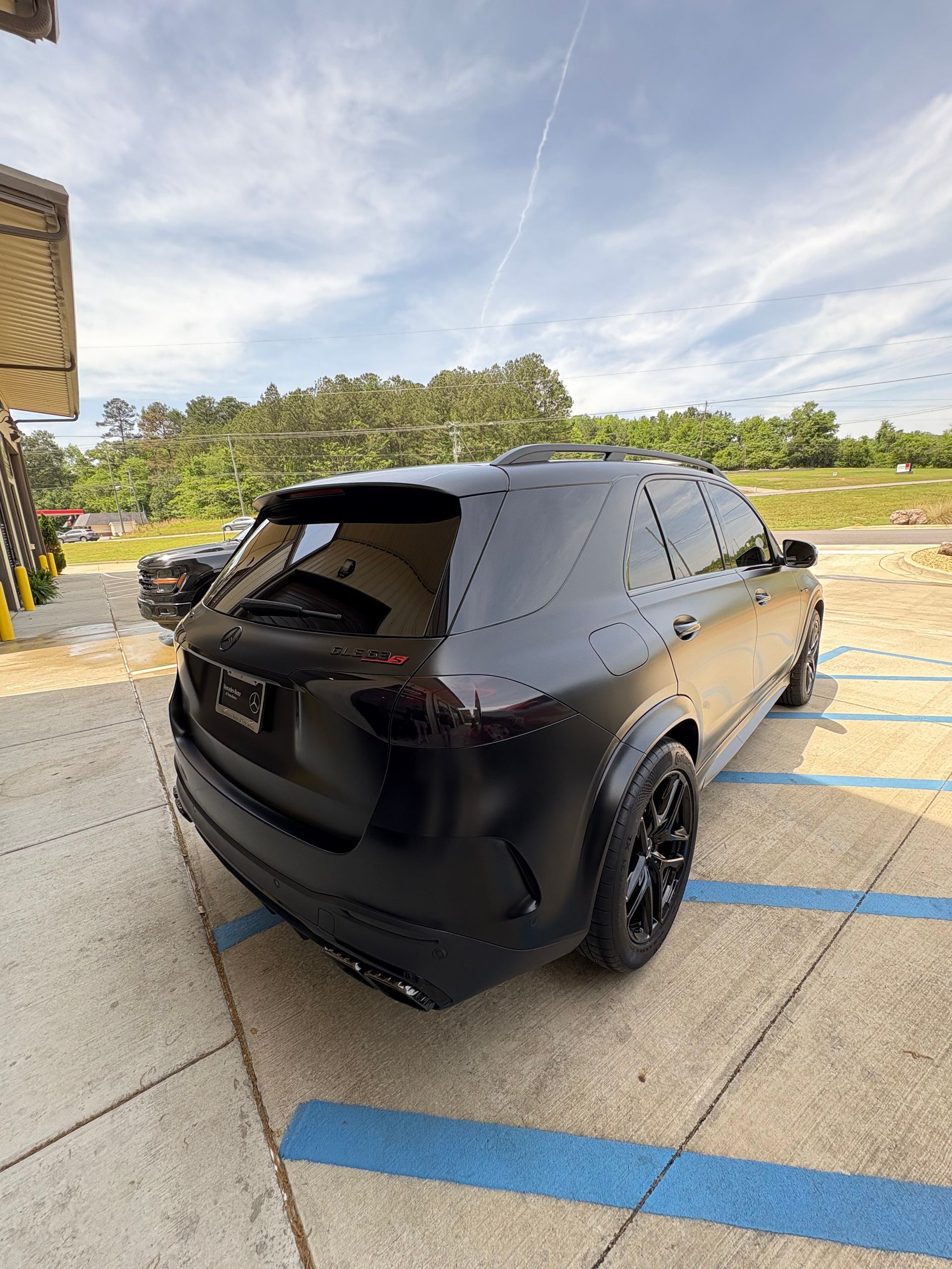 Black SUV parked on a paved surface under a cloudy sky. The car is sleek with blacked-out windows and rims.