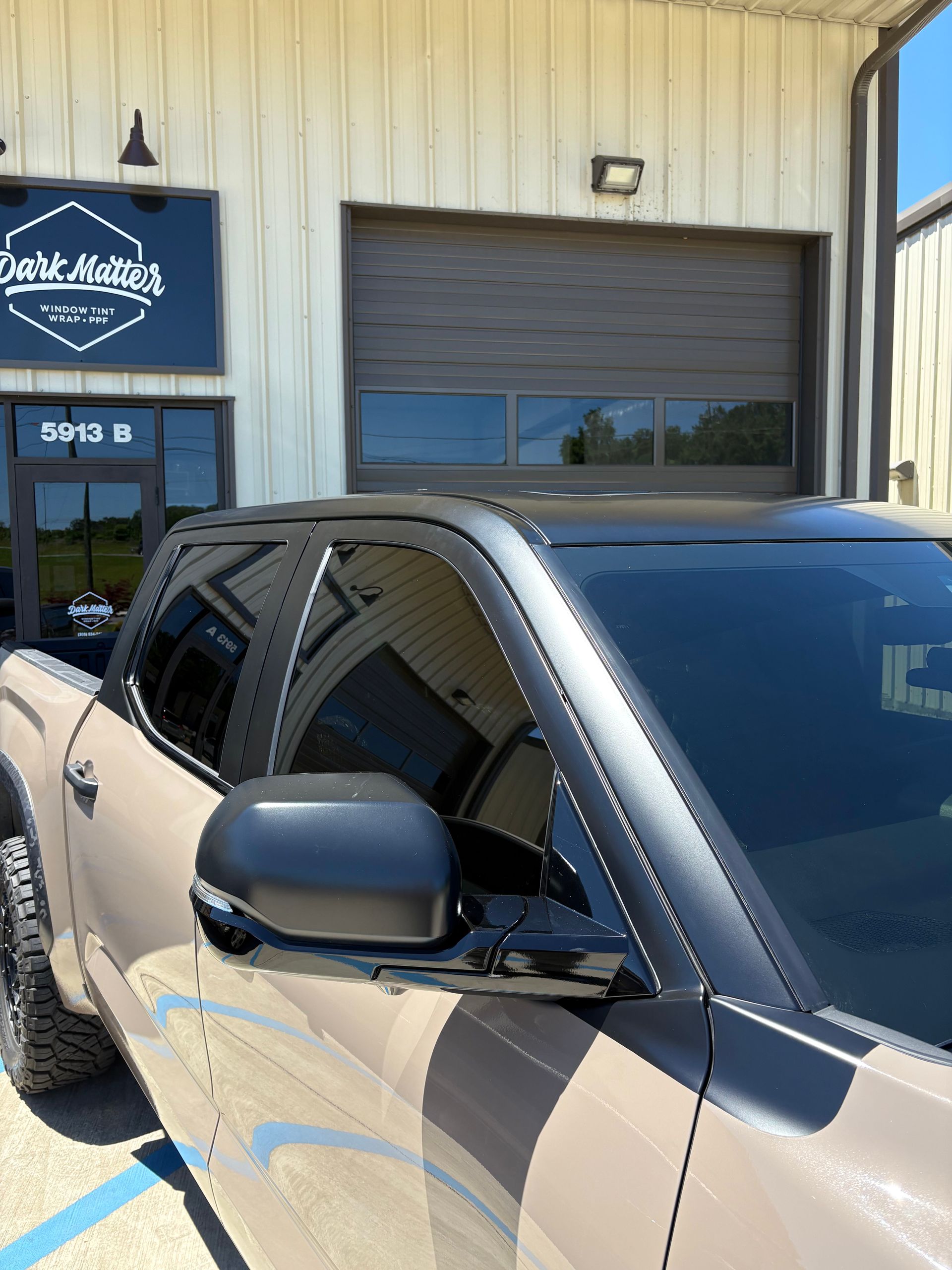 Tan pickup truck with tinted windows parked outside a business with a black door.