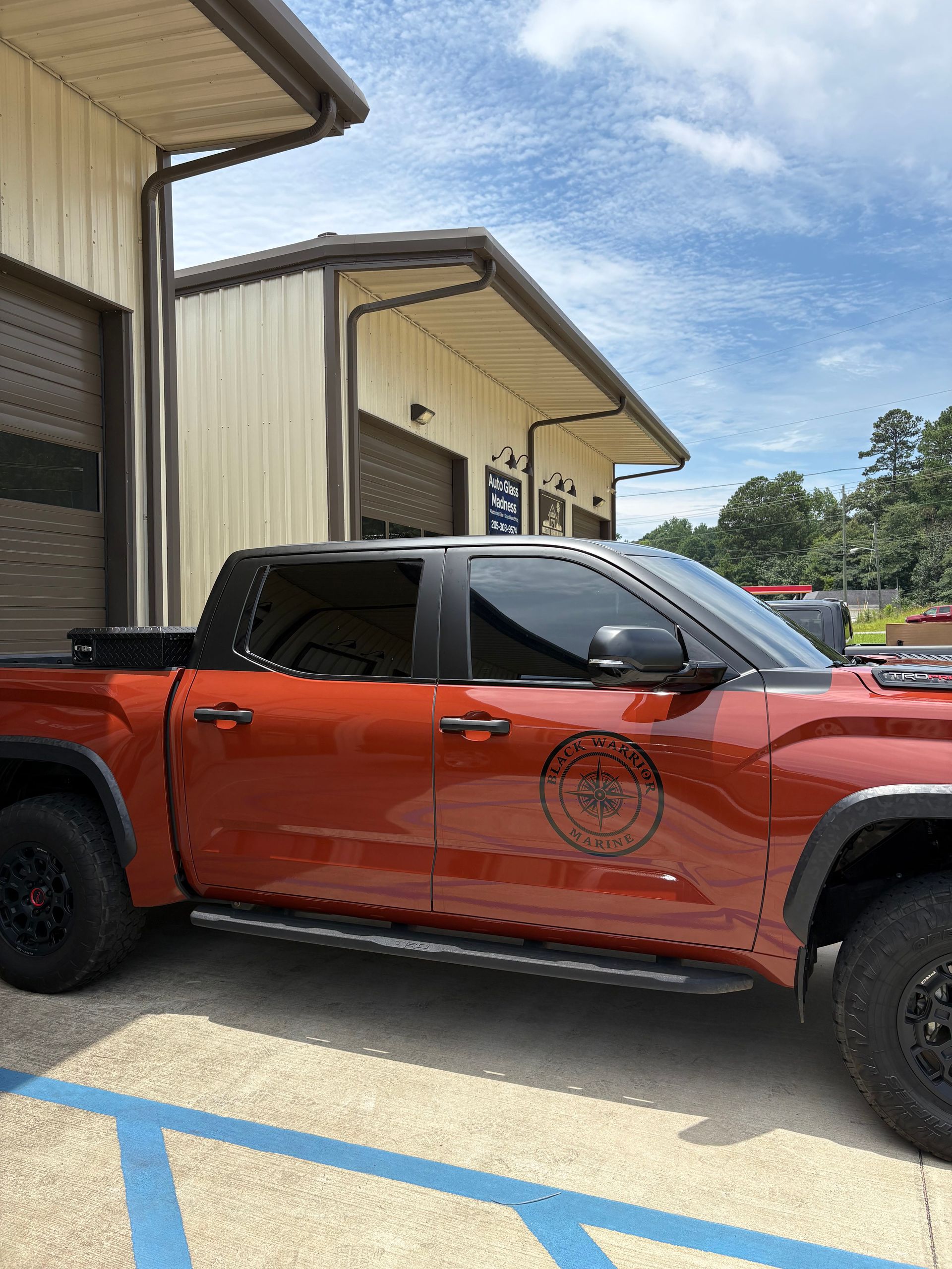 Red pickup truck parked in front of a tan building with brown trim under a partly cloudy sky.