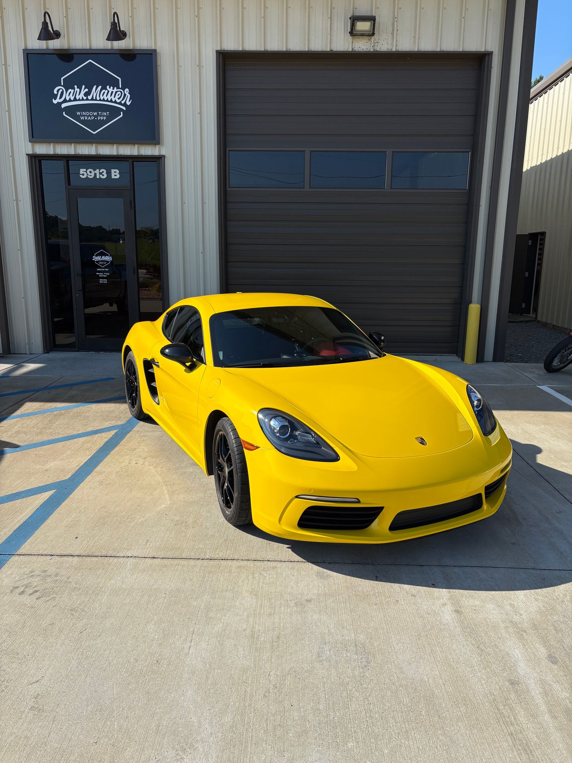 Yellow Porsche sports car parked outside a building with a garage door and sign.