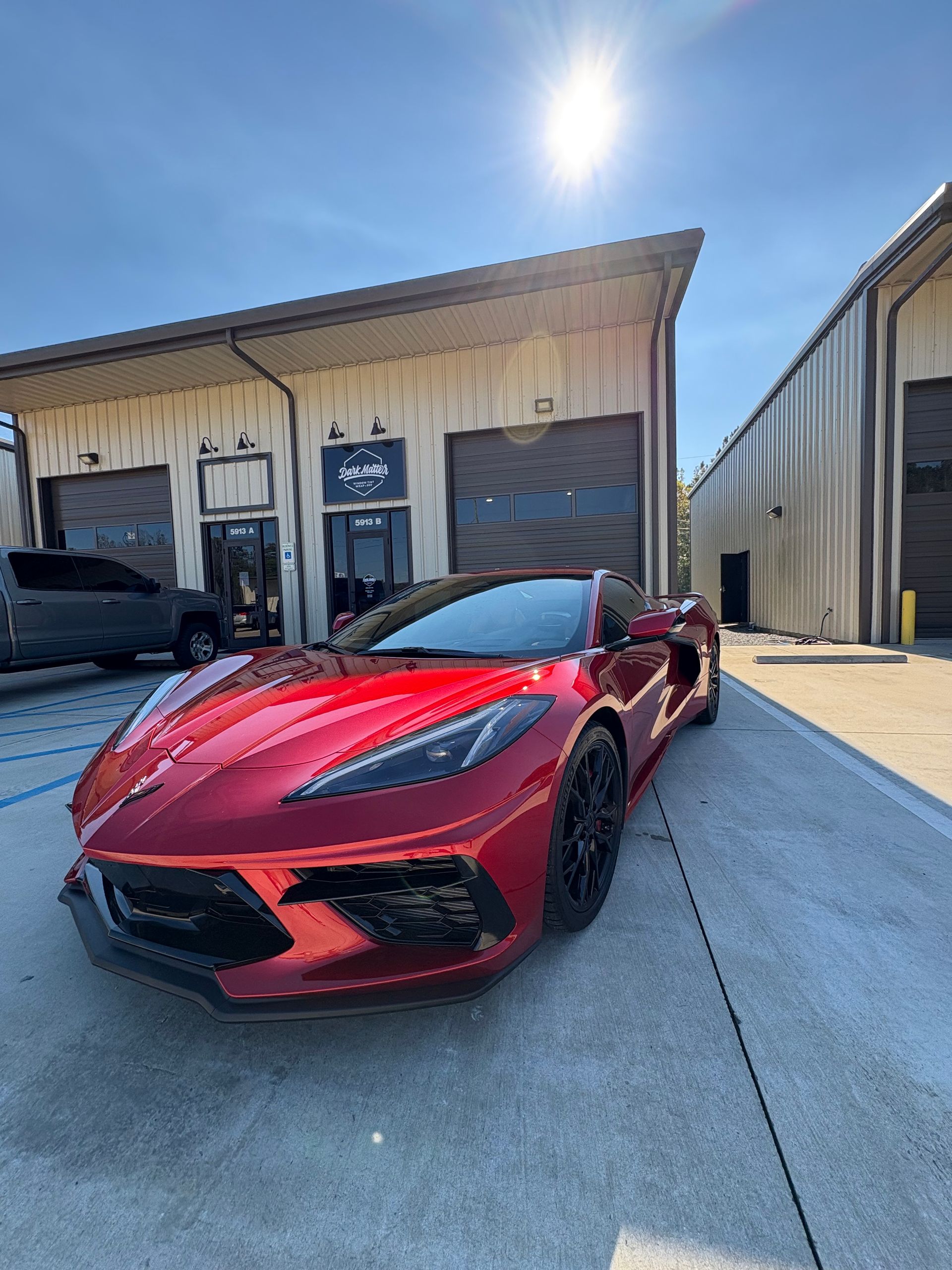 Red Chevrolet Corvette parked in front of a building with garage doors, under a sunny sky.