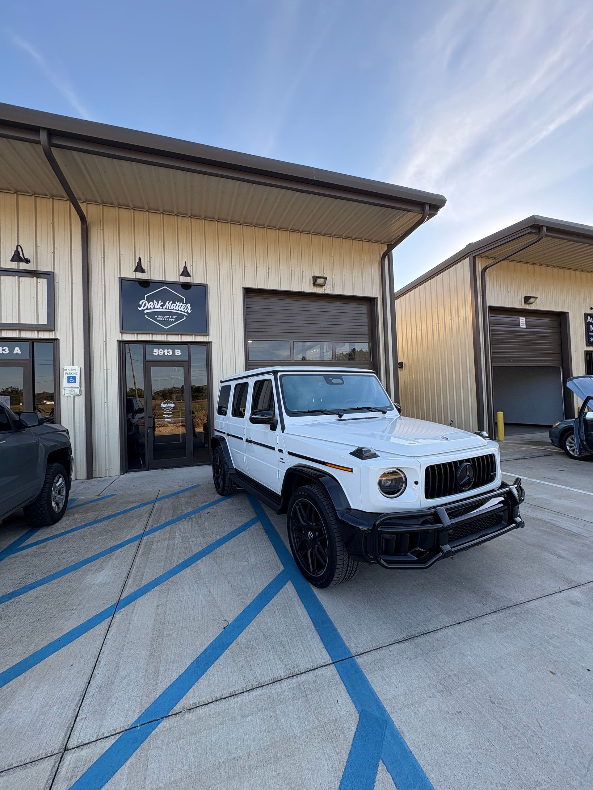 White SUV parked outside a shop with blue stripes on the ground.