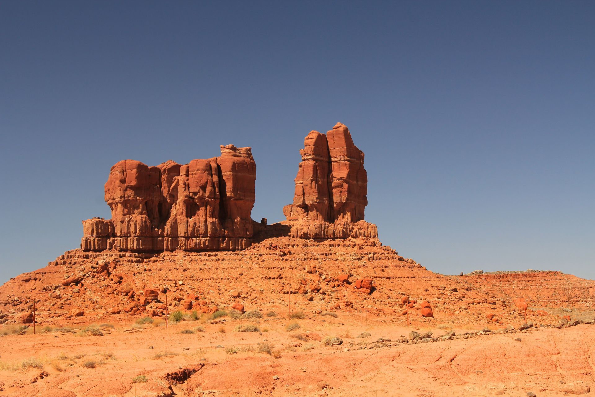 Two large, red sandstone rock formations stand against a clear, deep blue sky in a desert landscape.