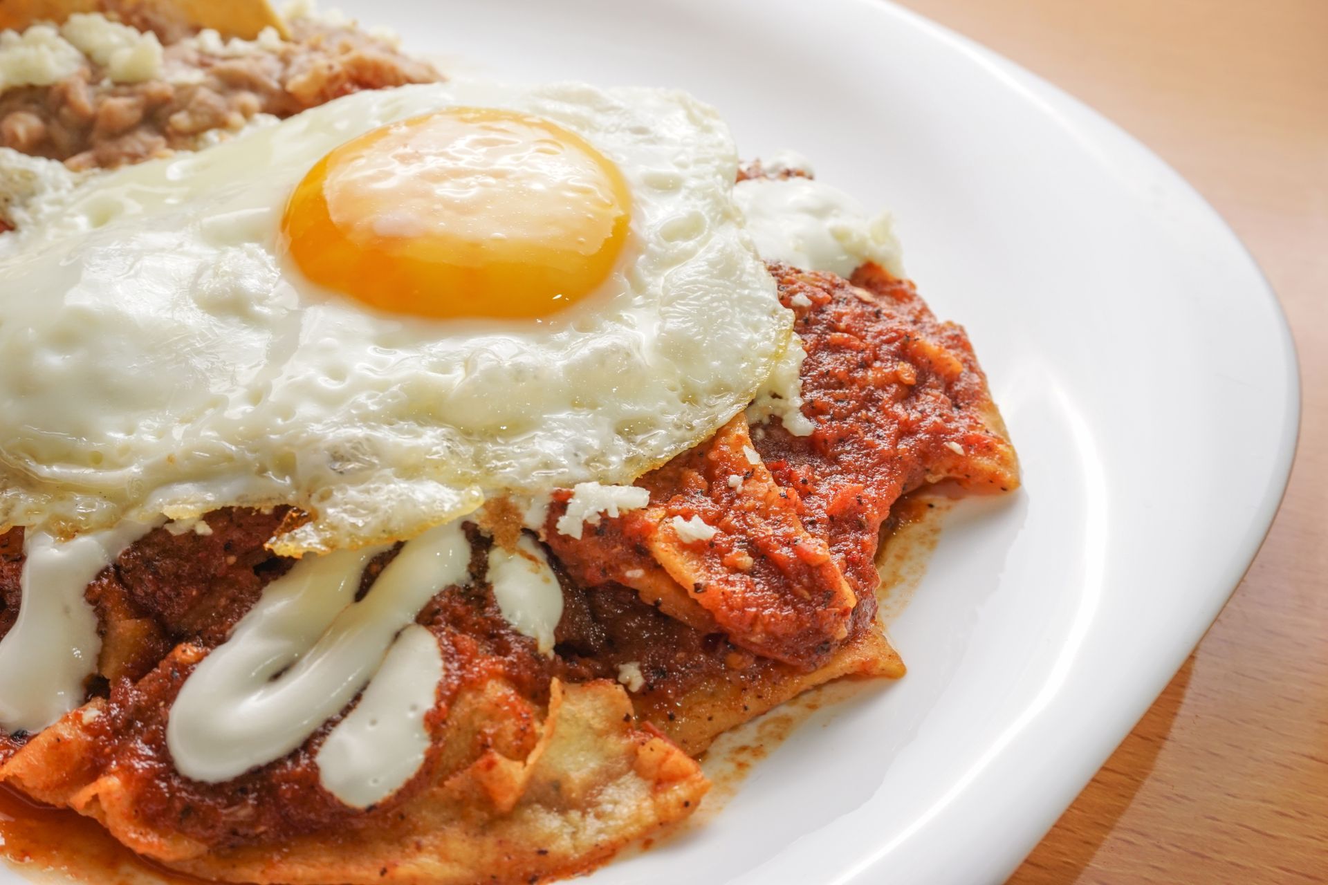 A plate of chilaquiles topped with a sunny-side-up egg, red salsa, sour cream, and a side of refried beans.