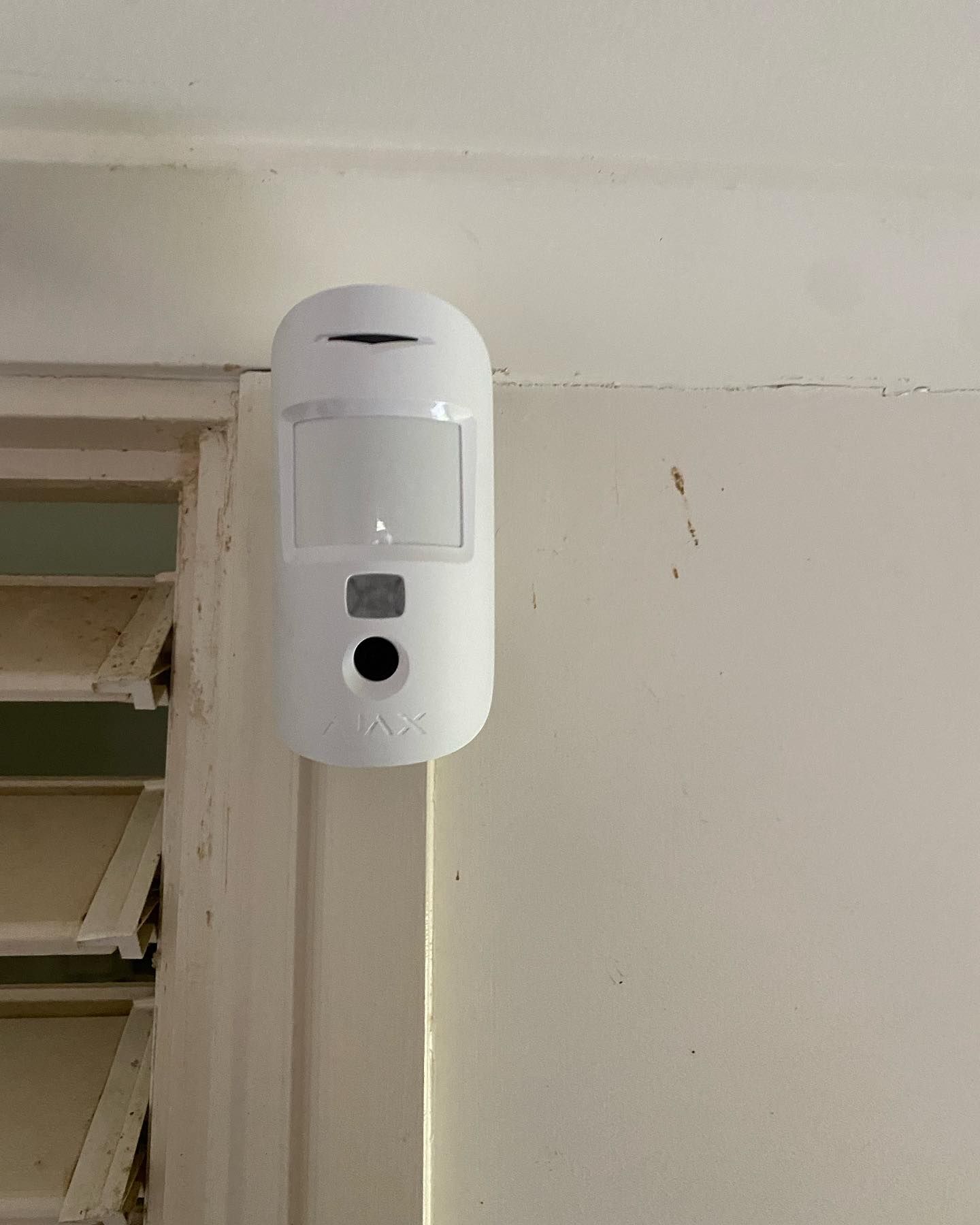 A White Motion Sensor is Mounted on a White Wall Next to a Door — DGC Tech Solutions In Tablelands, QLD