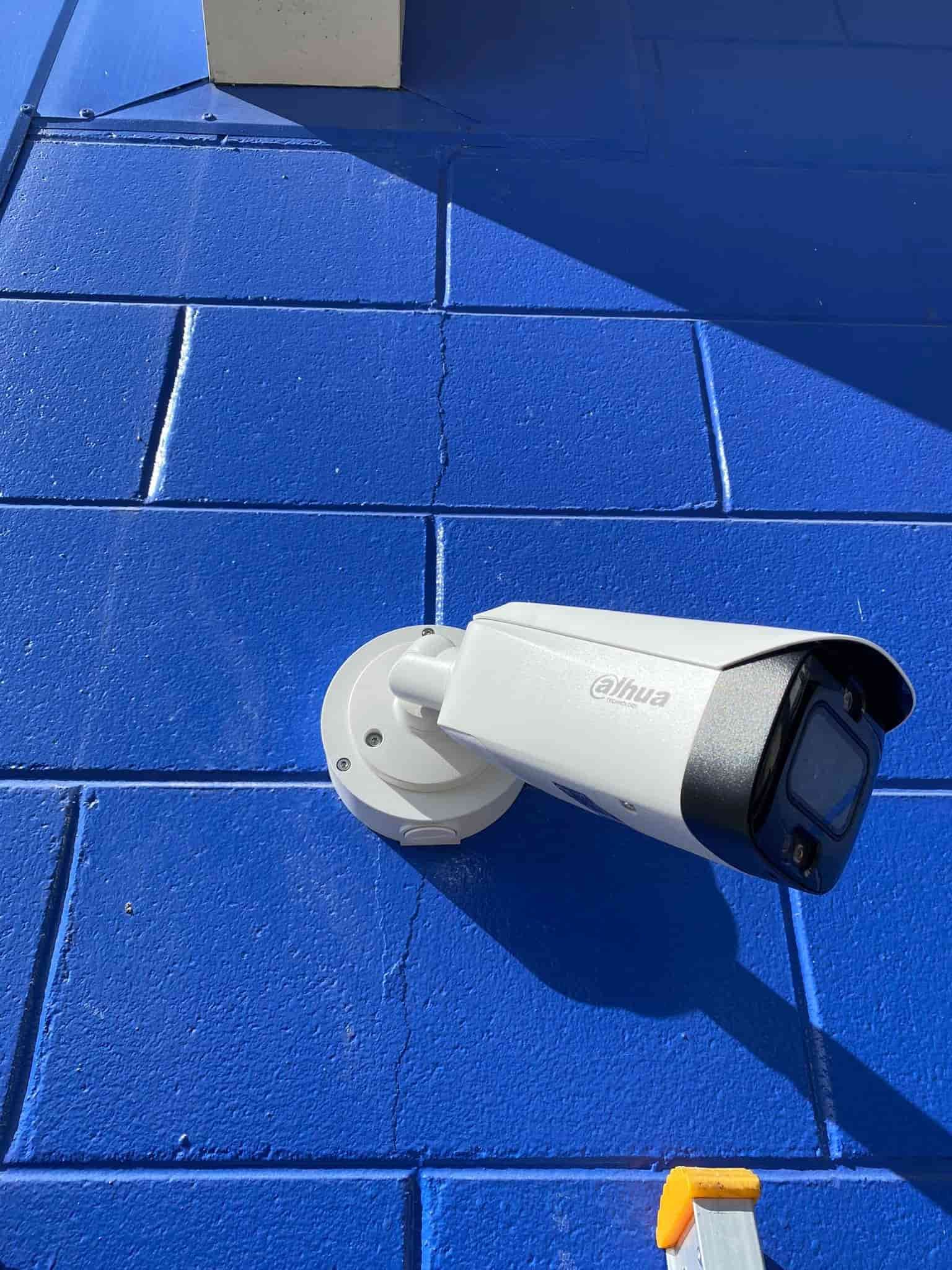 A Security Camera is Mounted on a Blue Brick Wall — DGC Tech Solutions In Cooktown, QLD