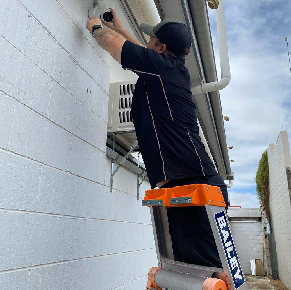 A Man is Standing on a Bailey Ladder Working on a Building — DGC Tech Solutions In Mareeba, QLD