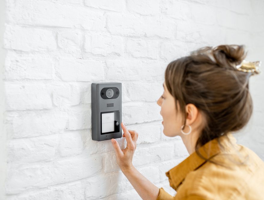 A Woman is Pressing a Button on a Doorbell on a White Brick Wall — DGC Tech Solutions In Mareeba, QLD