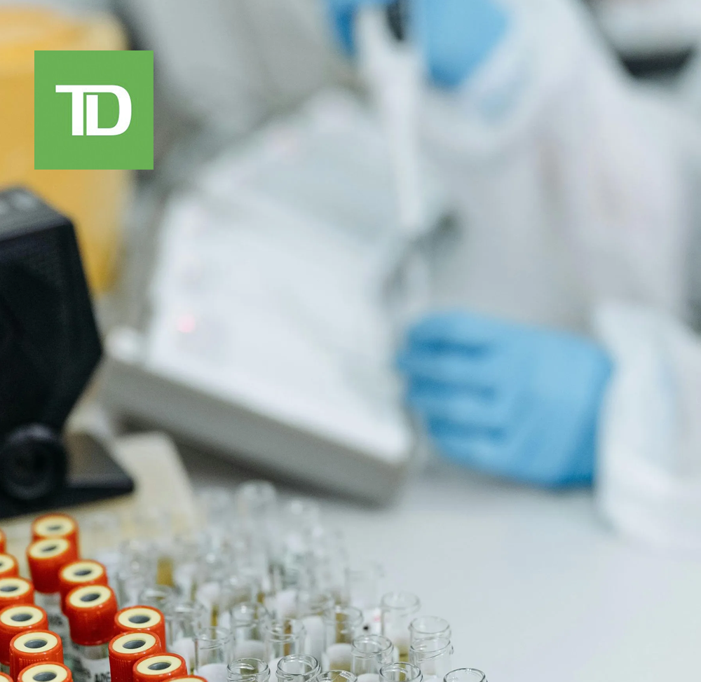 Laboratory setting with racks of vials, one being filled by a person in protective gear and gloves.