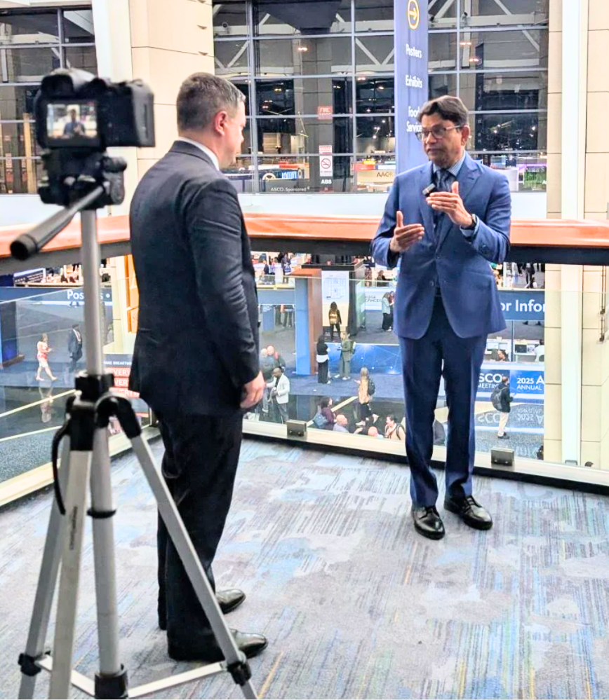 A man in a suit is talking to another man in front of a camera