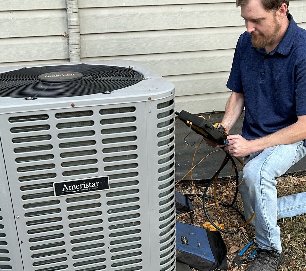 A technician inspects an Ameristar air conditioner with a meter outside a building.