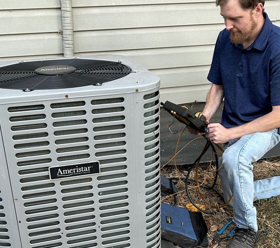 A technician inspects an Ameristar air conditioner with a meter outside a building.