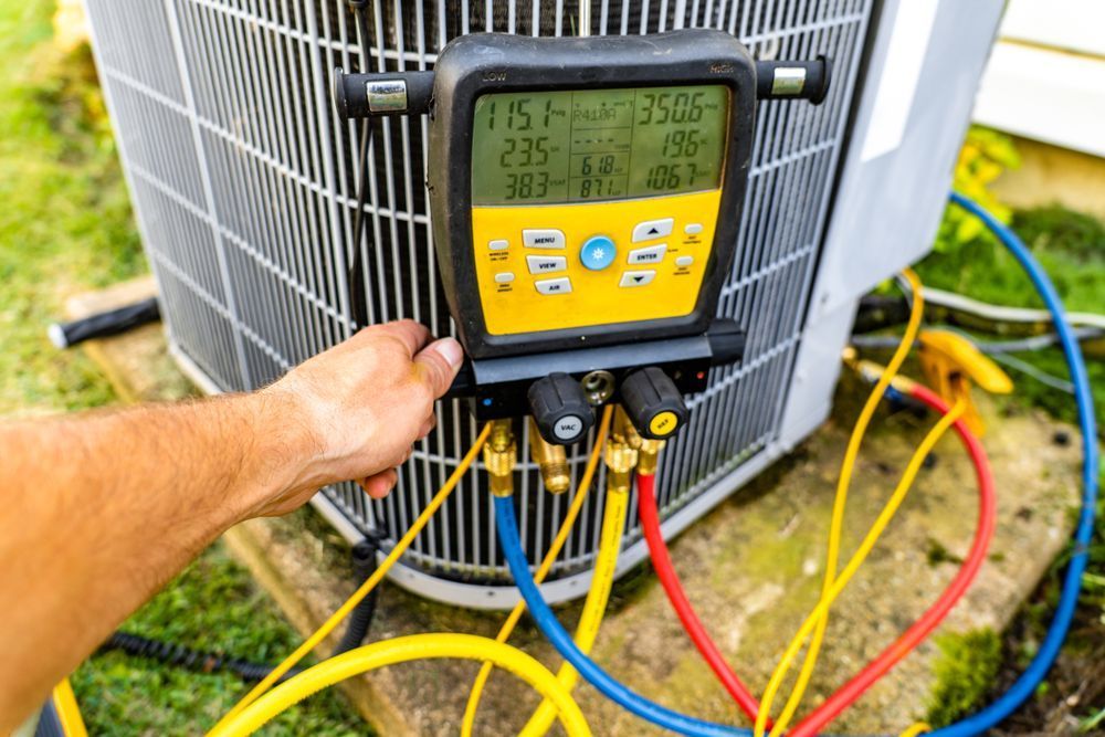 HVAC technician using a gauge manifold on an air conditioning unit; yellow, blue, and red hoses connected.