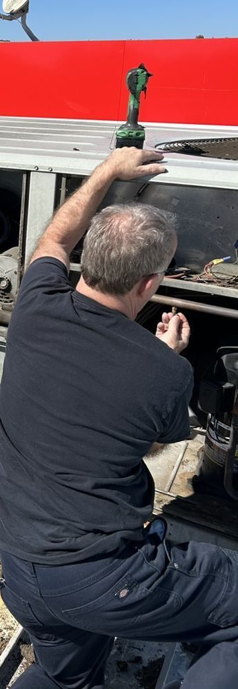 A person in dark clothing works on a vehicle under a red structure, holding a small tool.
