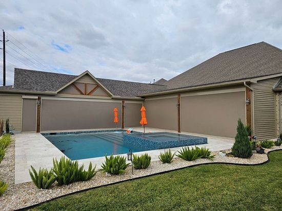 There is a large swimming pool in the backyard of a house with motorized shades