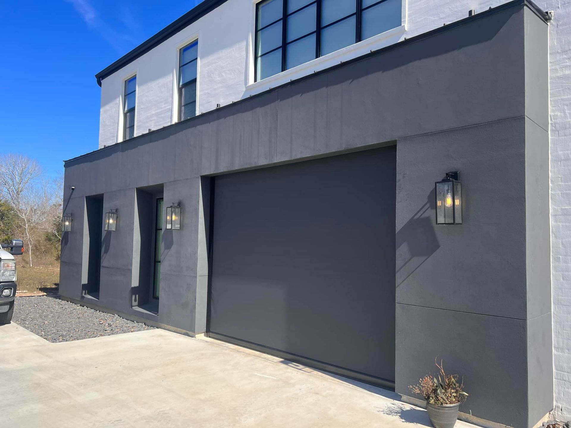 A large house with a gray garage door and a potted plant in front of it.