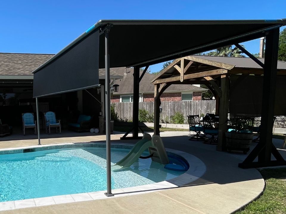 There is a large swimming pool in the backyard of a house with a motorized pergola