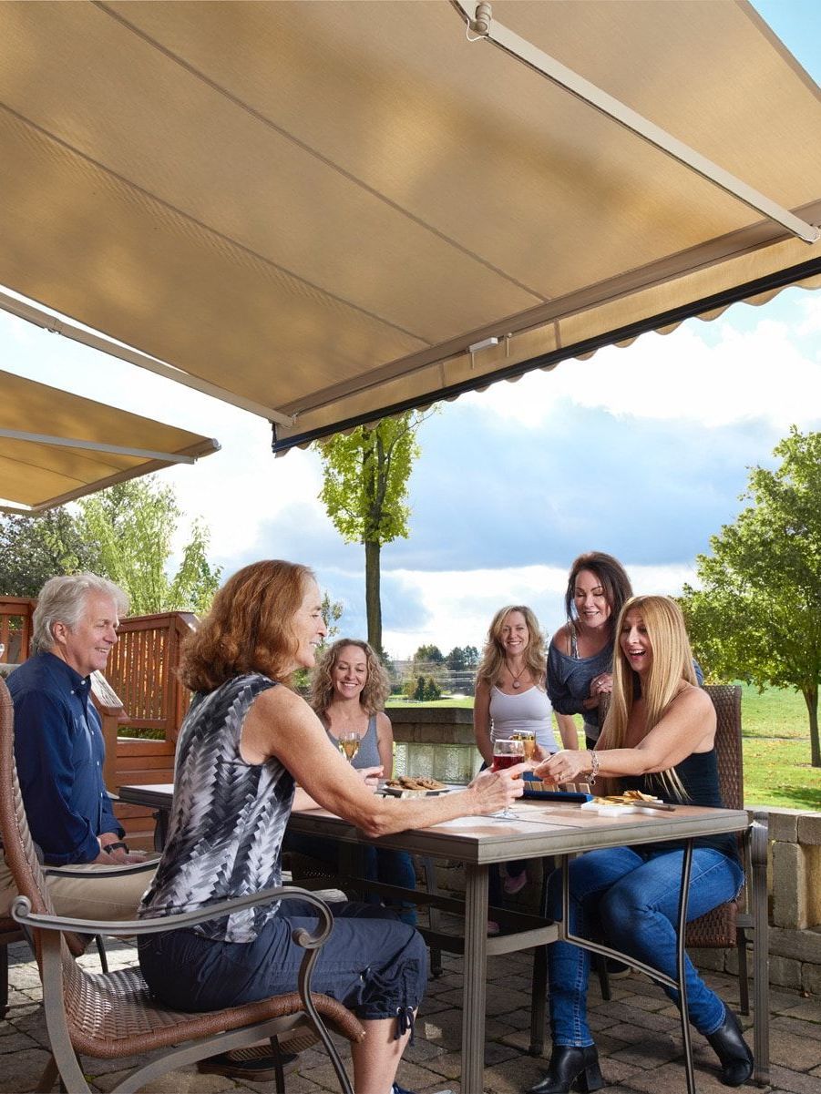 A happy group of people are sitting at a table under a motorized awning.