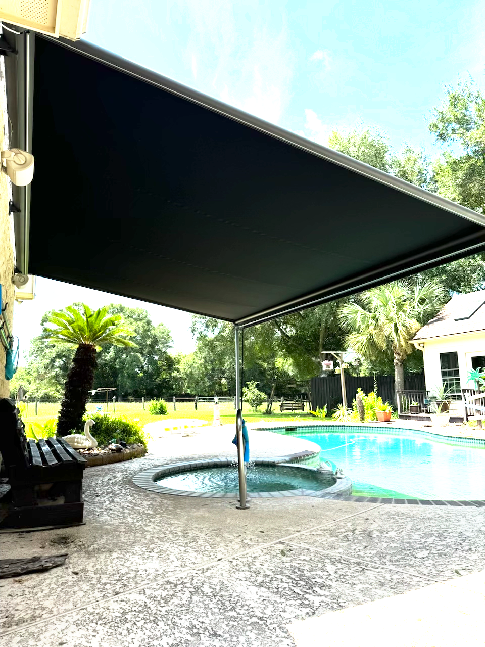 A black awning is covering a swimming pool in a backyard.