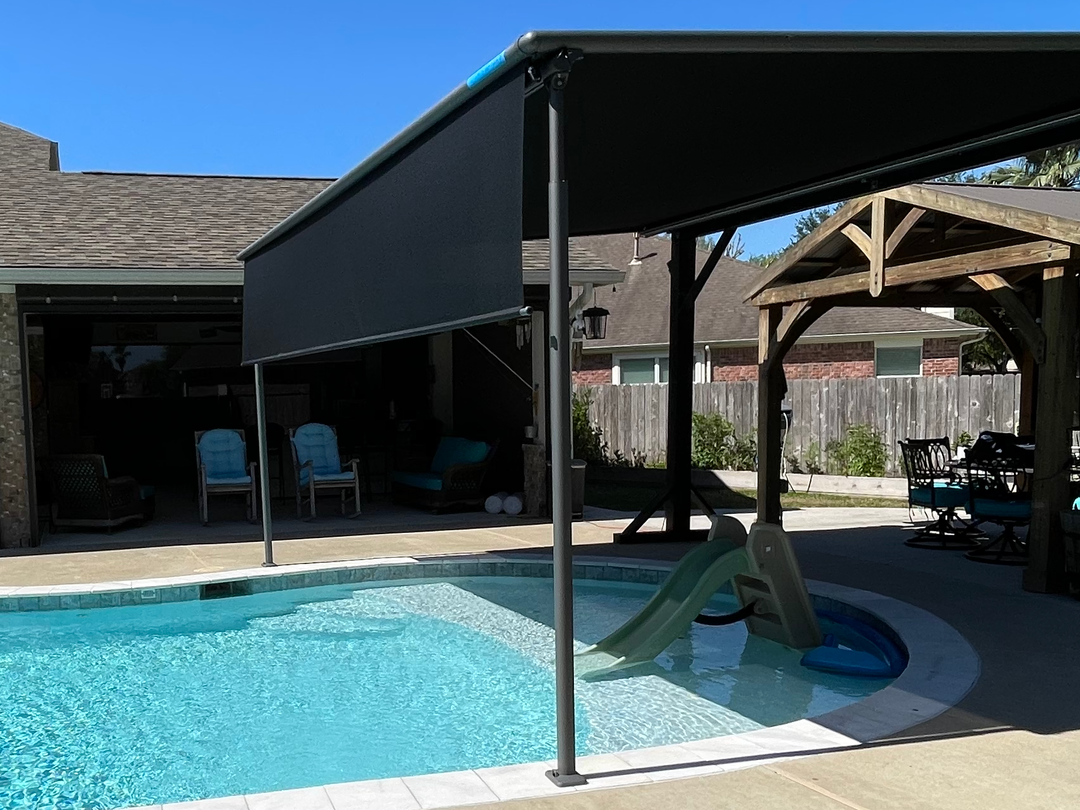 There is a large swimming pool in the backyard of a house with a motorized pergola