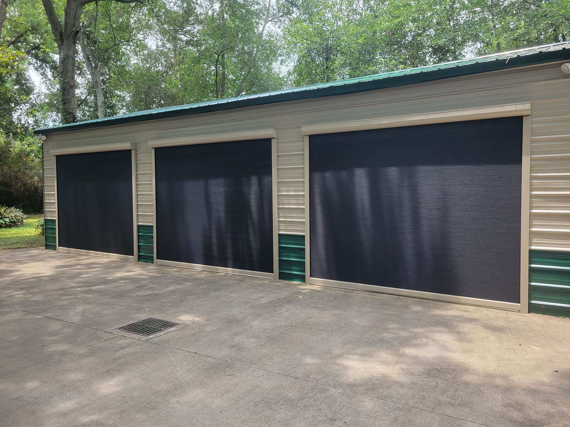 A garage with three black garage doors and trees in the background.